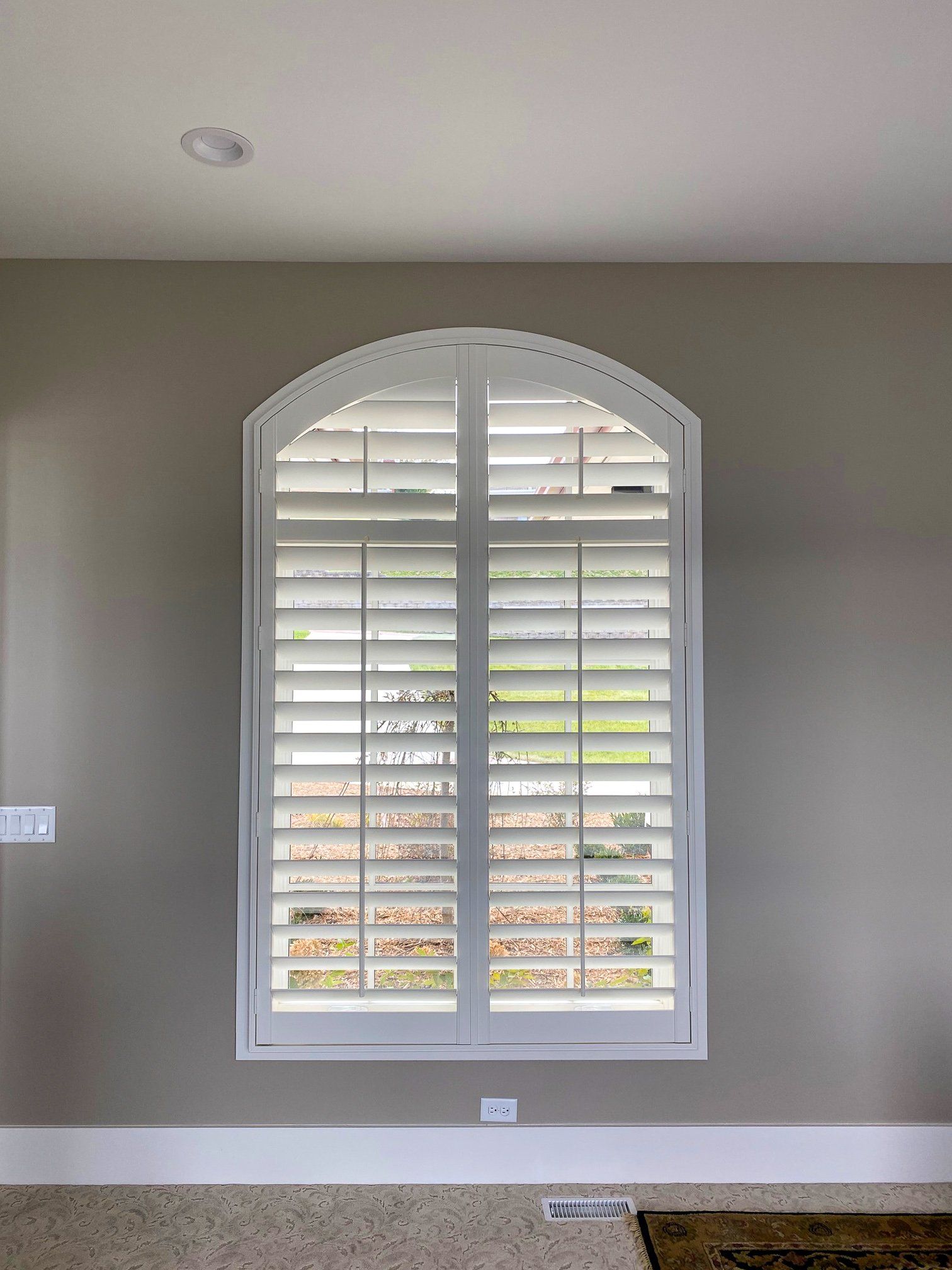 A large window with arched shutters in a living room.