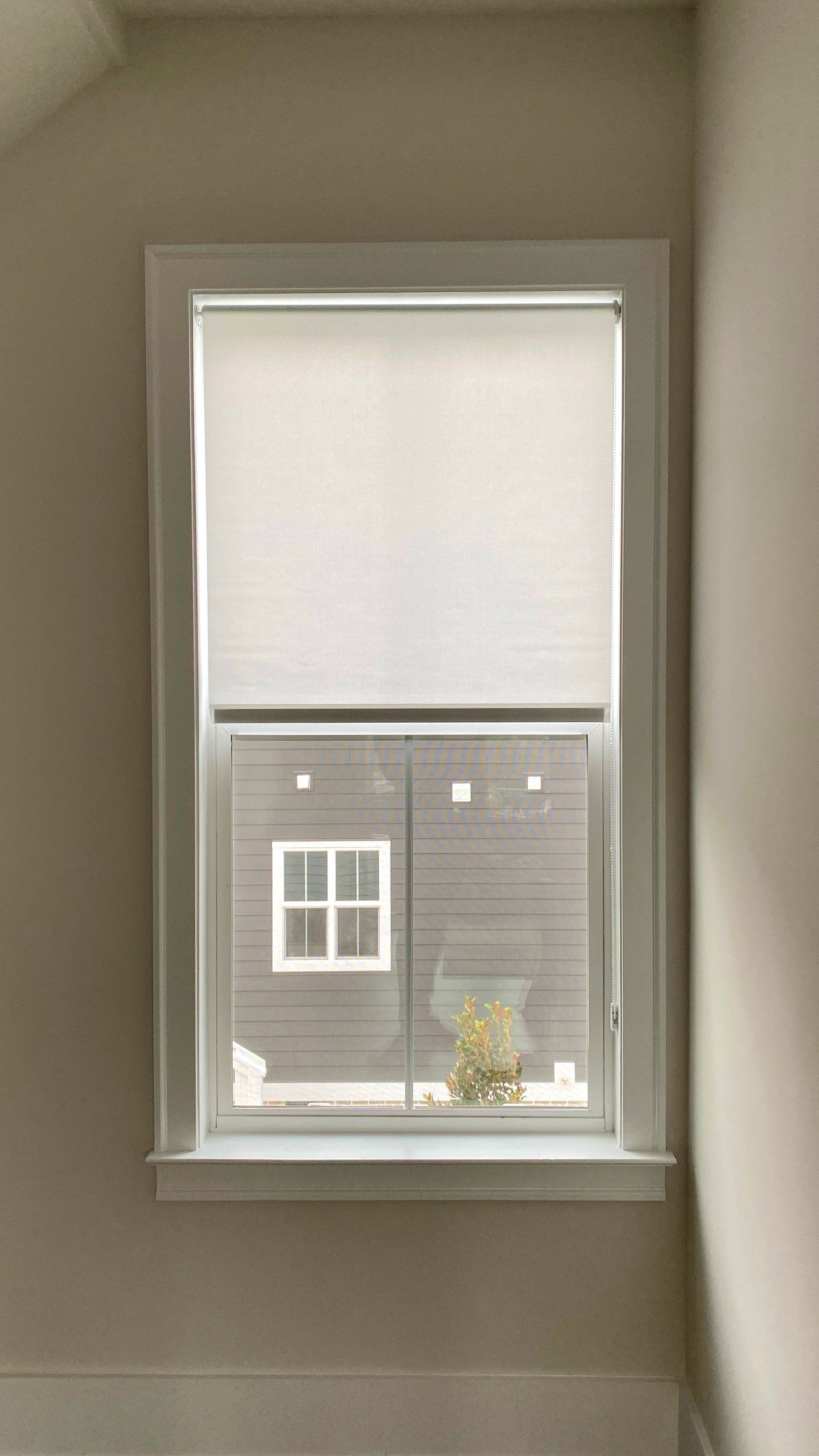 A window with white blinds in a room with a view of a house.