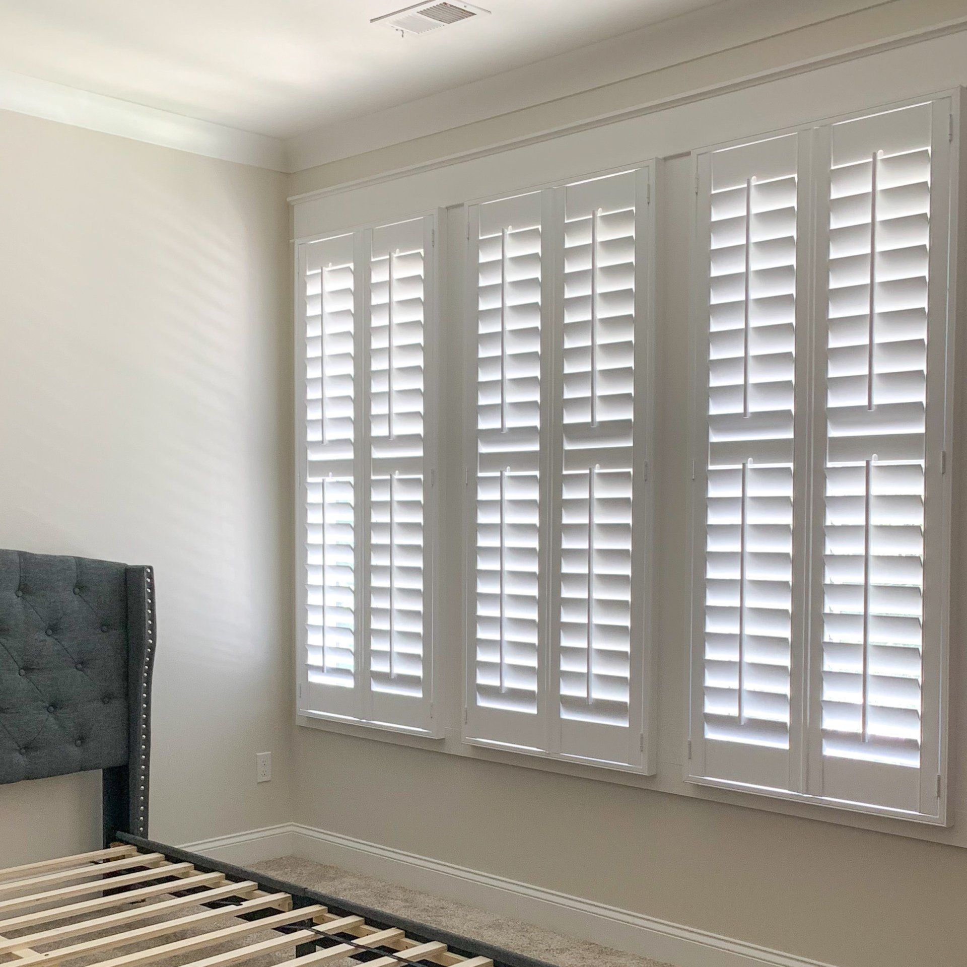 A bedroom with white shutters on the windows and a bed.