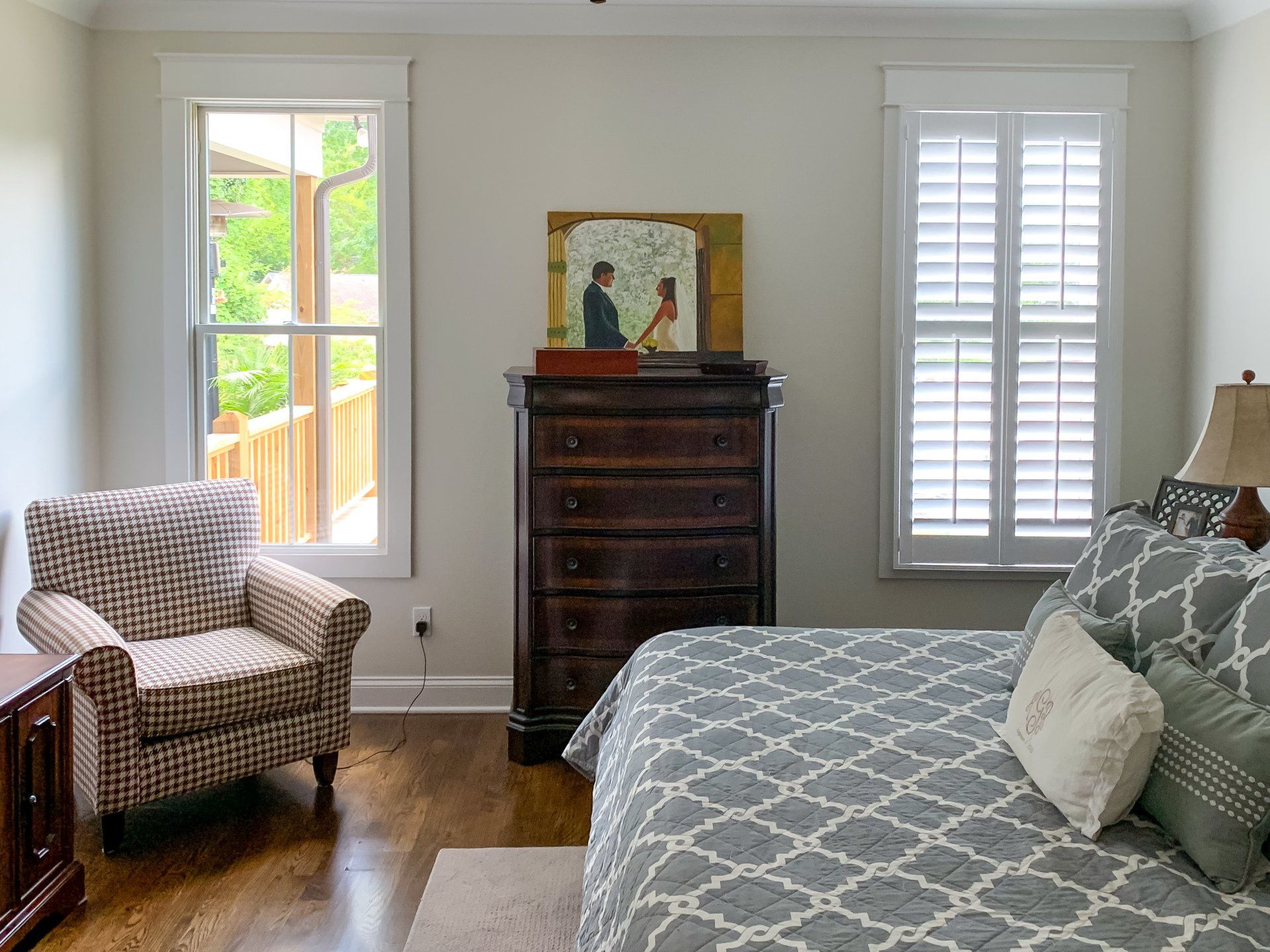 A bedroom with a bed , chair , dresser and two windows.
