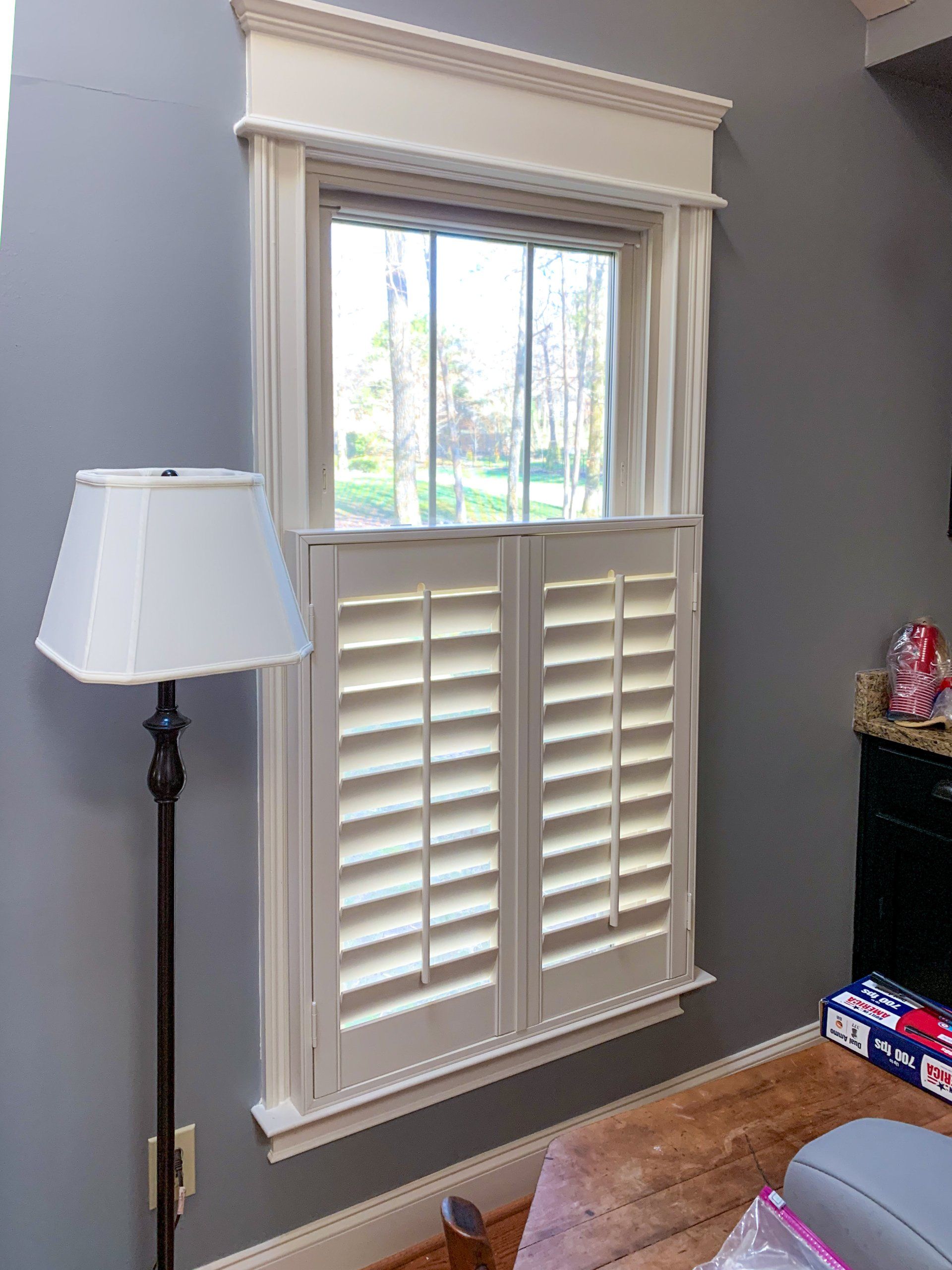 A living room with a lamp and a window with shutters.