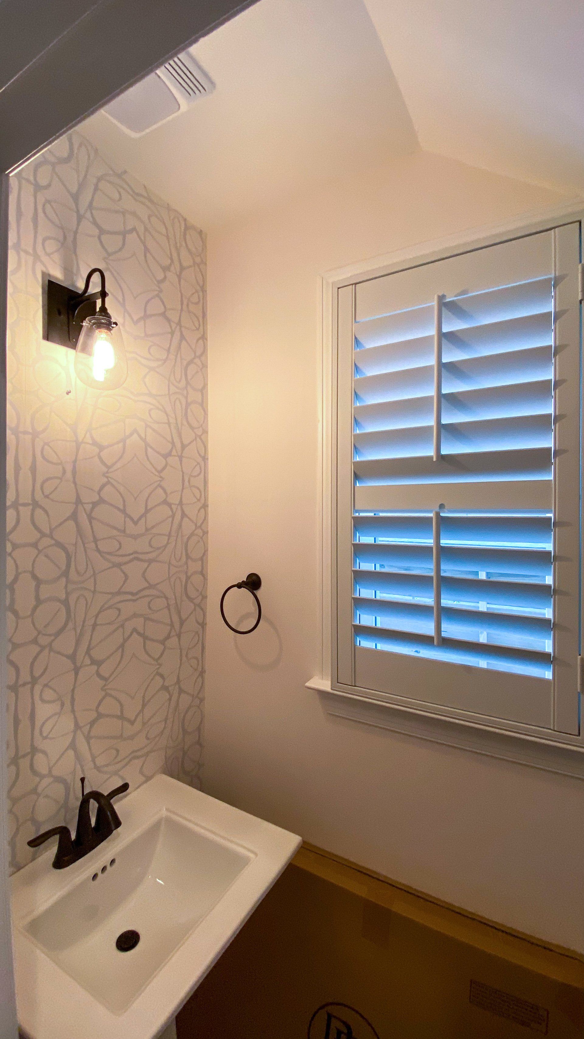 A bathroom with a sink and a window with shutters.