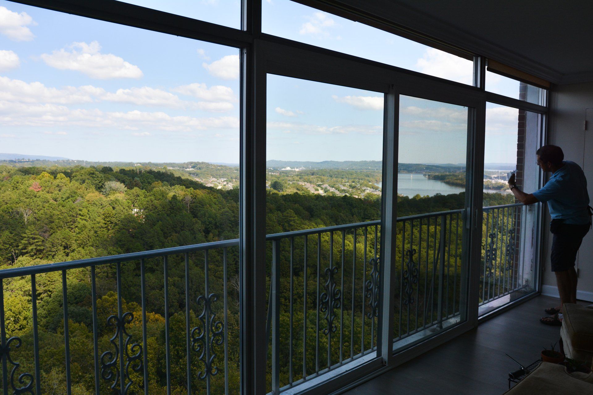 A man is standing in front of a large window overlooking a forest.