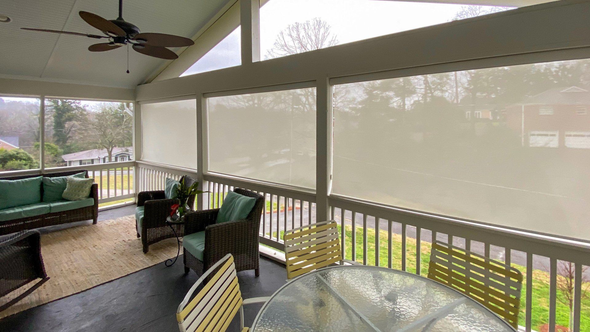 A screened in porch with a table and chairs and a ceiling fan.