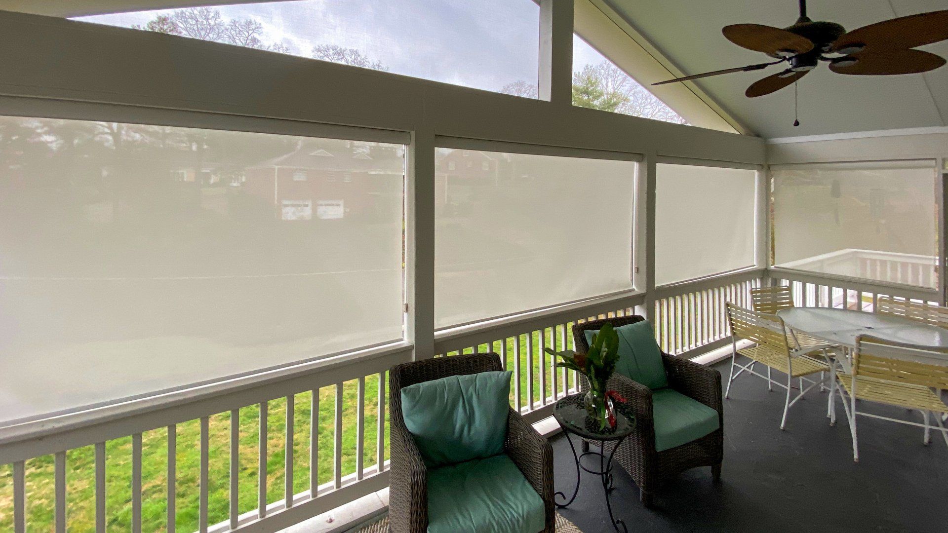 A screened in porch with a table and chairs and a ceiling fan.