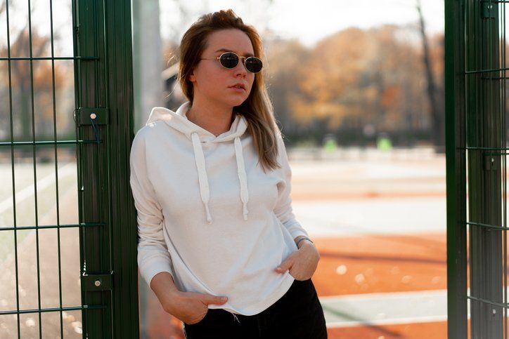 Outdoor close up portrait of young woman with long hair in sunglasses, dressed in a white sweater