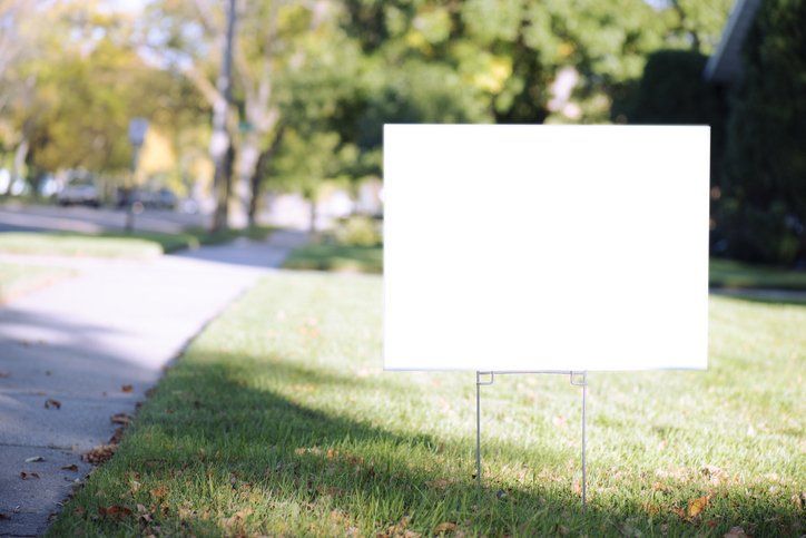 Yard sign on grass by sidewalk