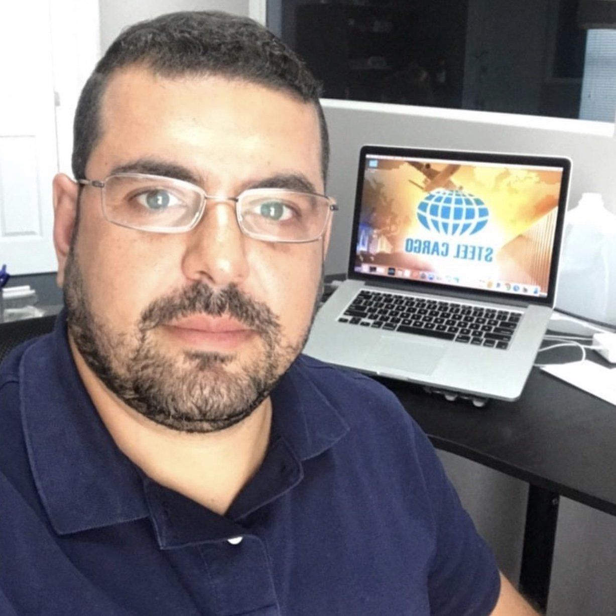 Um homem de óculos sentado em frente a um laptop com a palavra carga na tela