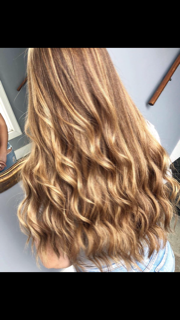 a woman with long wavy Balayage hair is standing in front of a mirror .