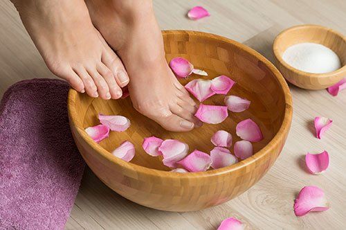 a woman is soaking her feet in a wooden bowl filled with rose petals .