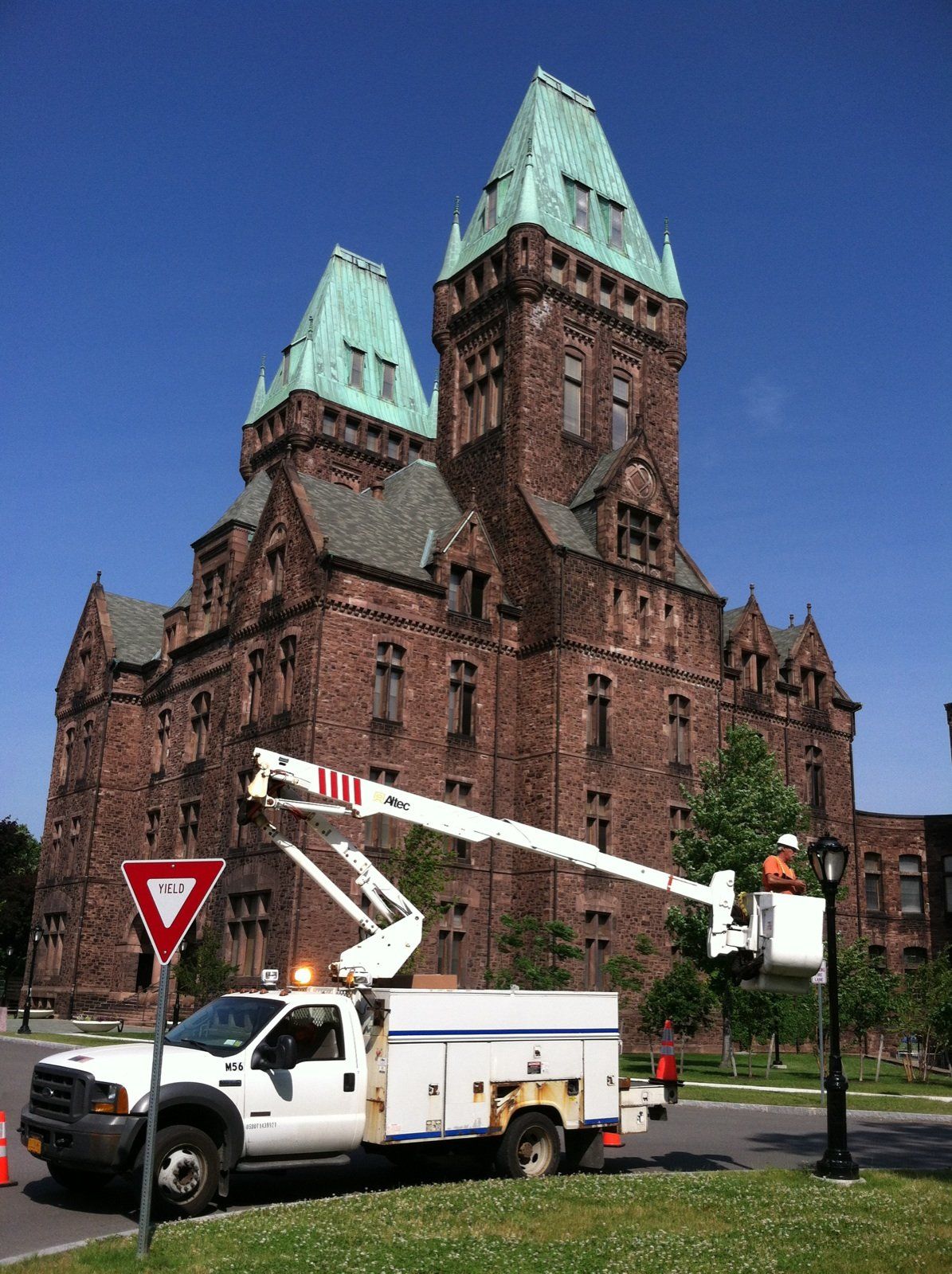 White utility truck with lift in front of a large, brown building with green-roofed towers.