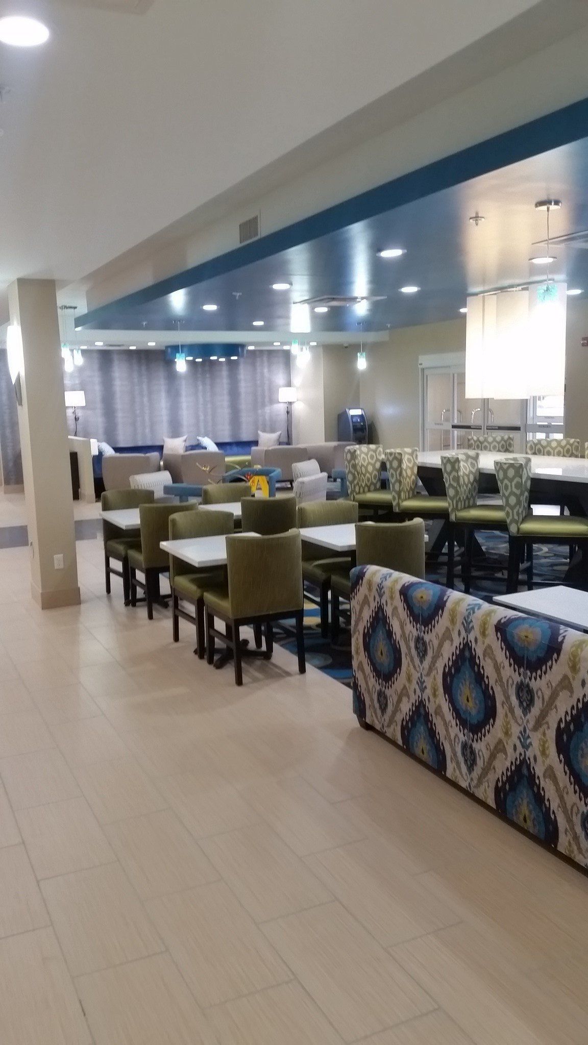 Lobby with tables and chairs, sofa, and a long table. Blue and cream color scheme, with overhead lighting.