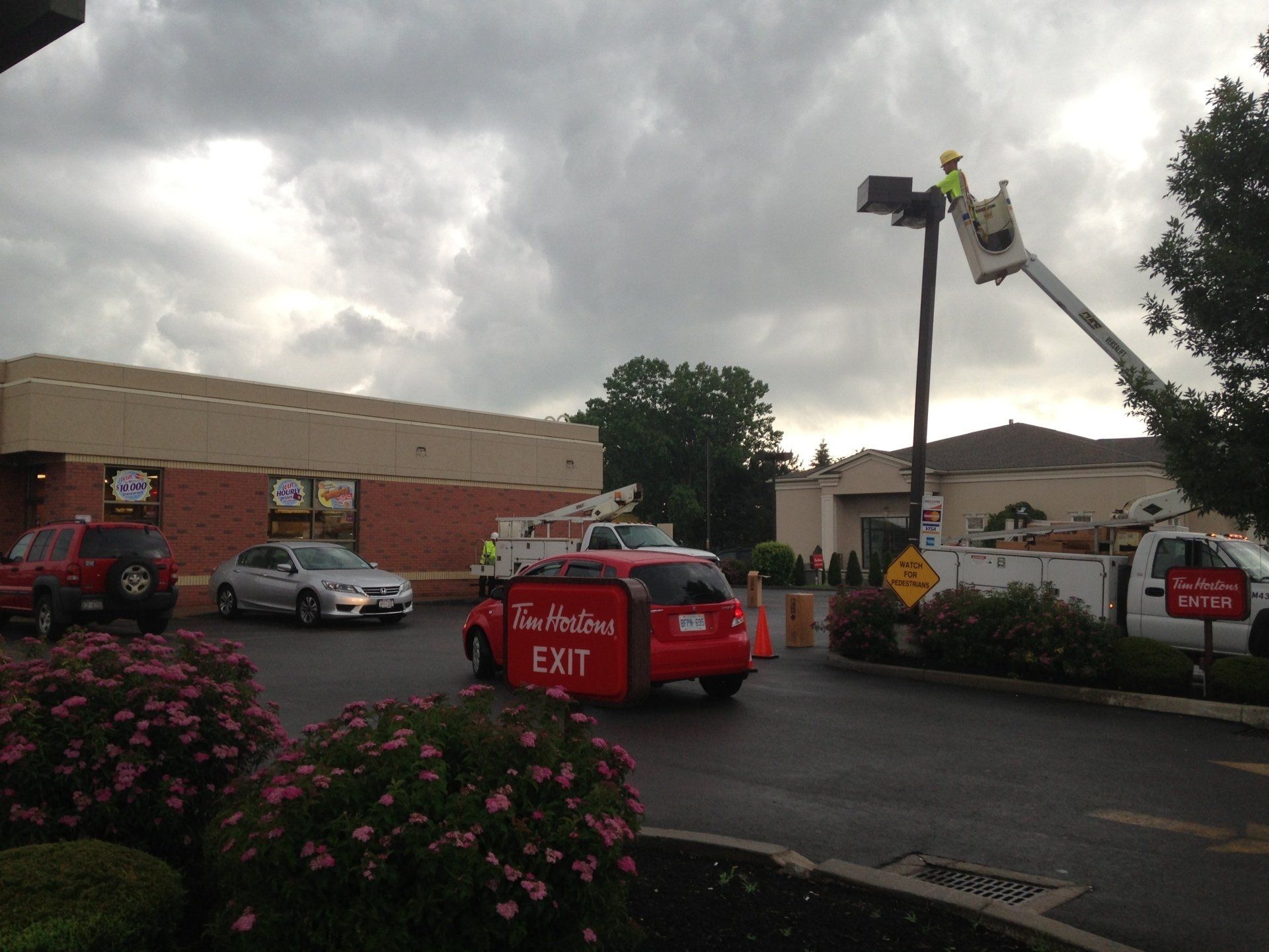 Tim Hortons drive-thru with a car exiting. A worker in a lift is working on a sign under a cloudy sky.