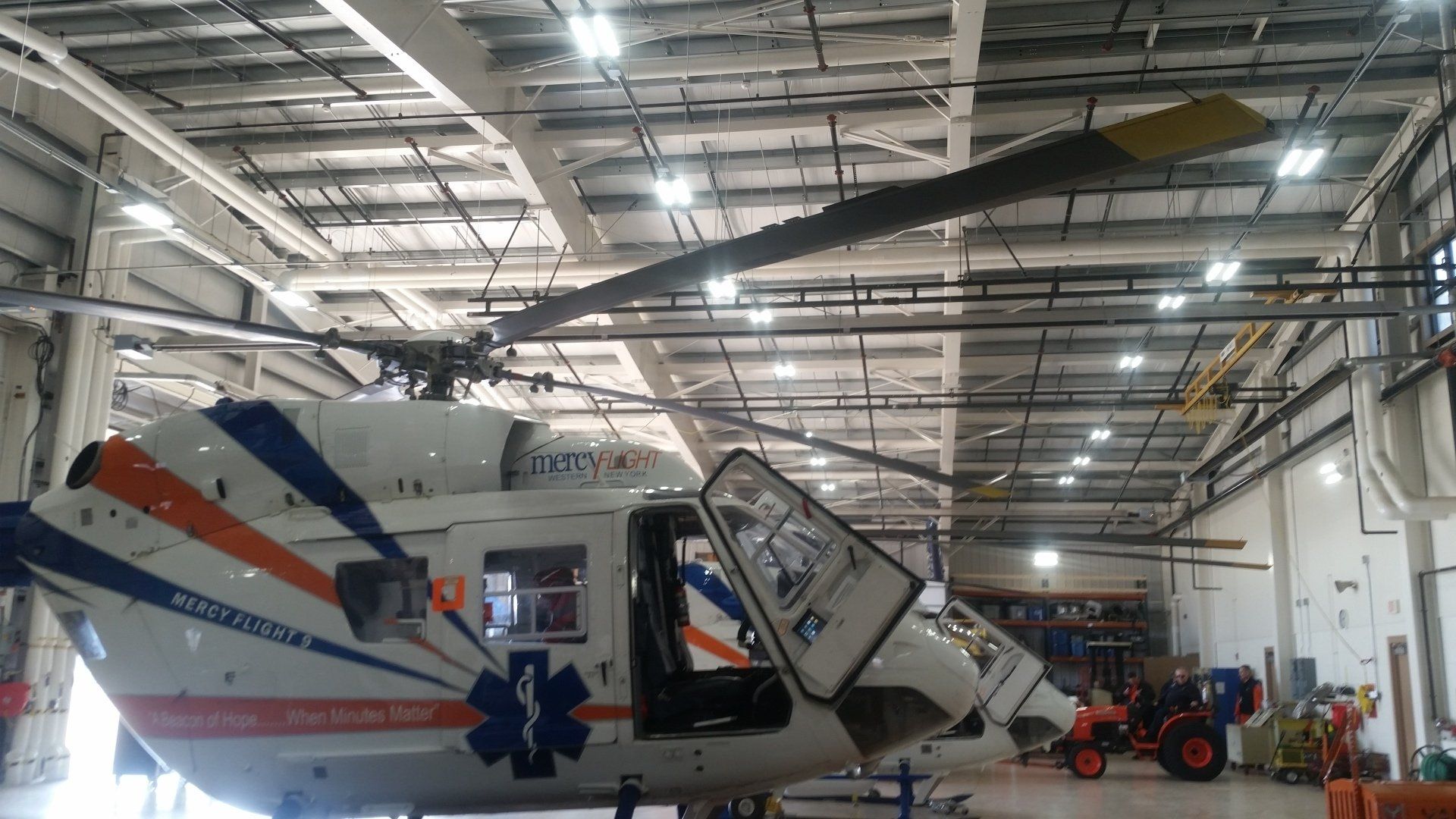 Helicopter inside a hangar with doors open; white, blue, and orange medical transport livery.