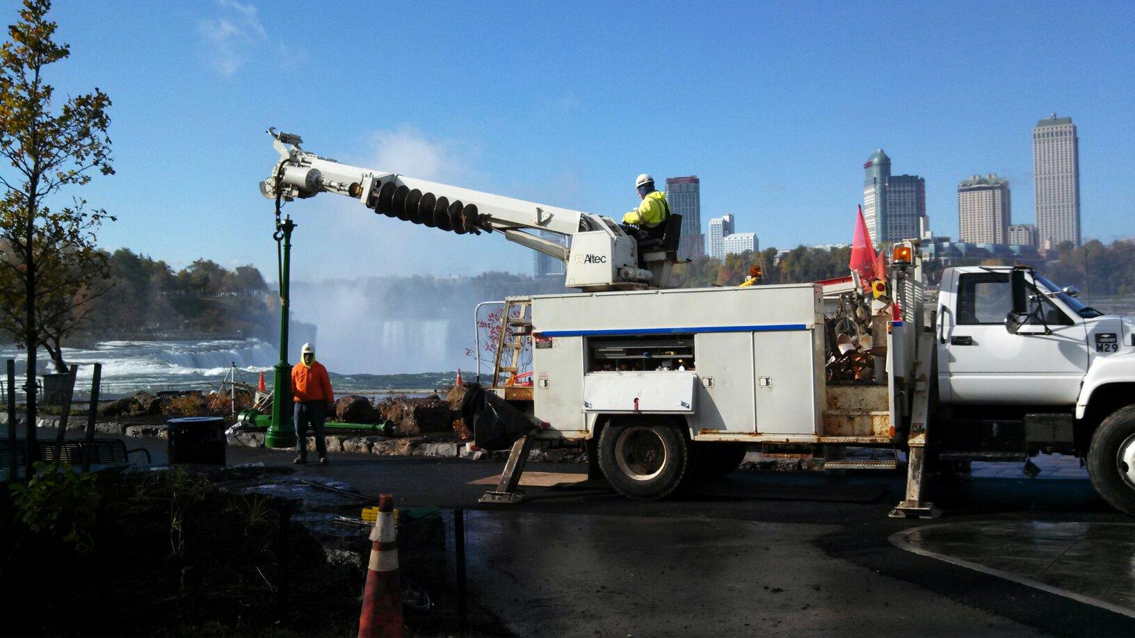 Truck with crane near Niagara Falls, workers in hard hats, clear sky.