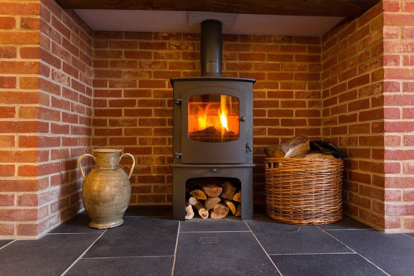 Roaring fire inside wood burning stove in brick fireplace with basket of cut wood ready for burning; Shutterstock ID 158889230; PO: N/A; Job: BULK; Client: N/A; Other: BULK
