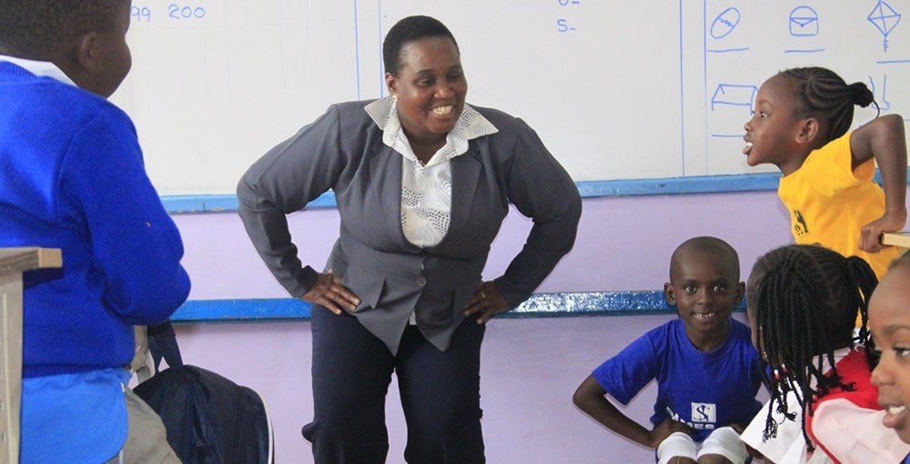 A woman is standing in front of a group of children in a classroom.