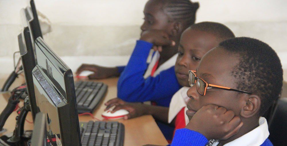 A group of children are sitting at a desk using computers.