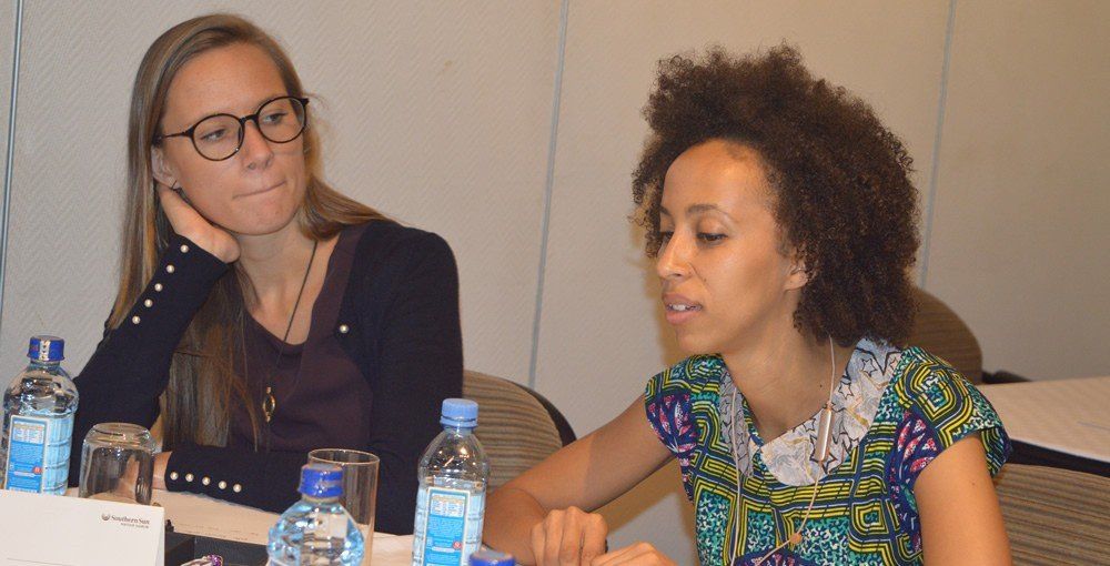 Two women are sitting at a table with bottles of water.