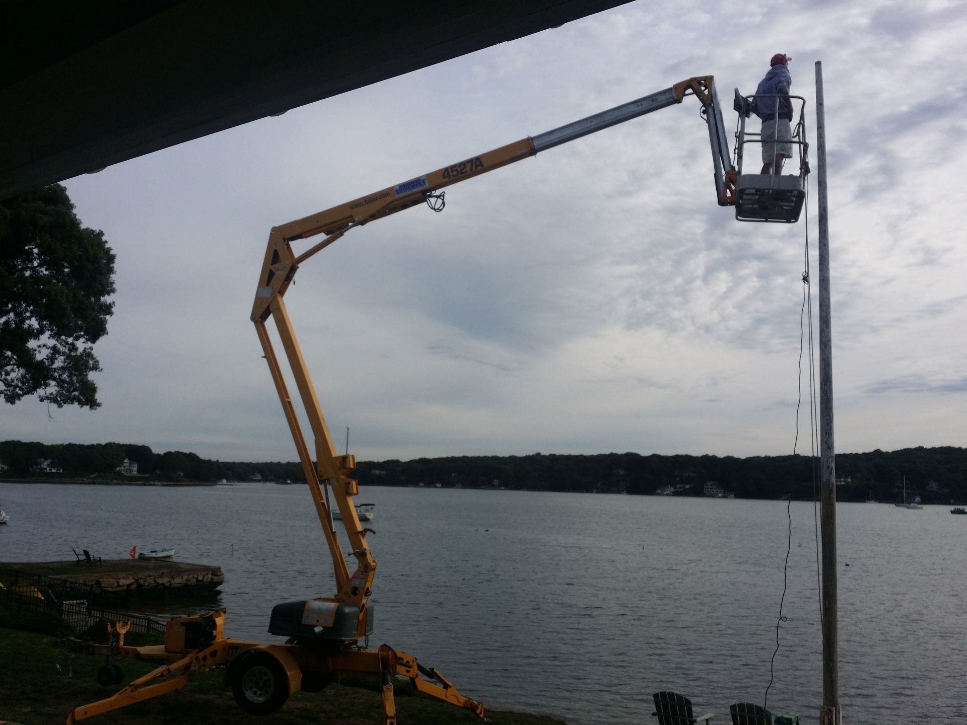 A person in a lift bucket working on a pole near a body of water.