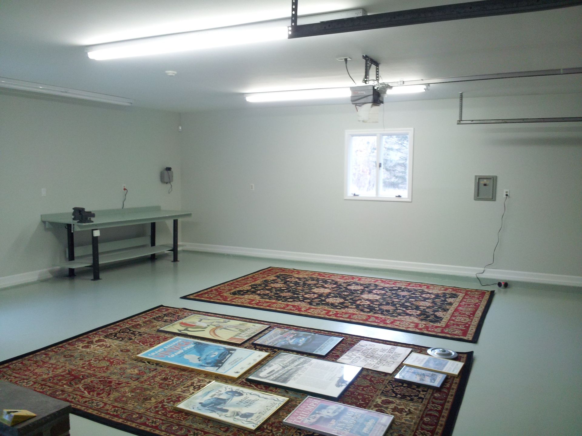 Empty garage with rugs and art laid out on the floor.