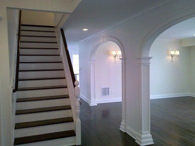Staircase leading up, with dark wood treads, to a white-walled hallway with archways, sconces and dark wood floors.