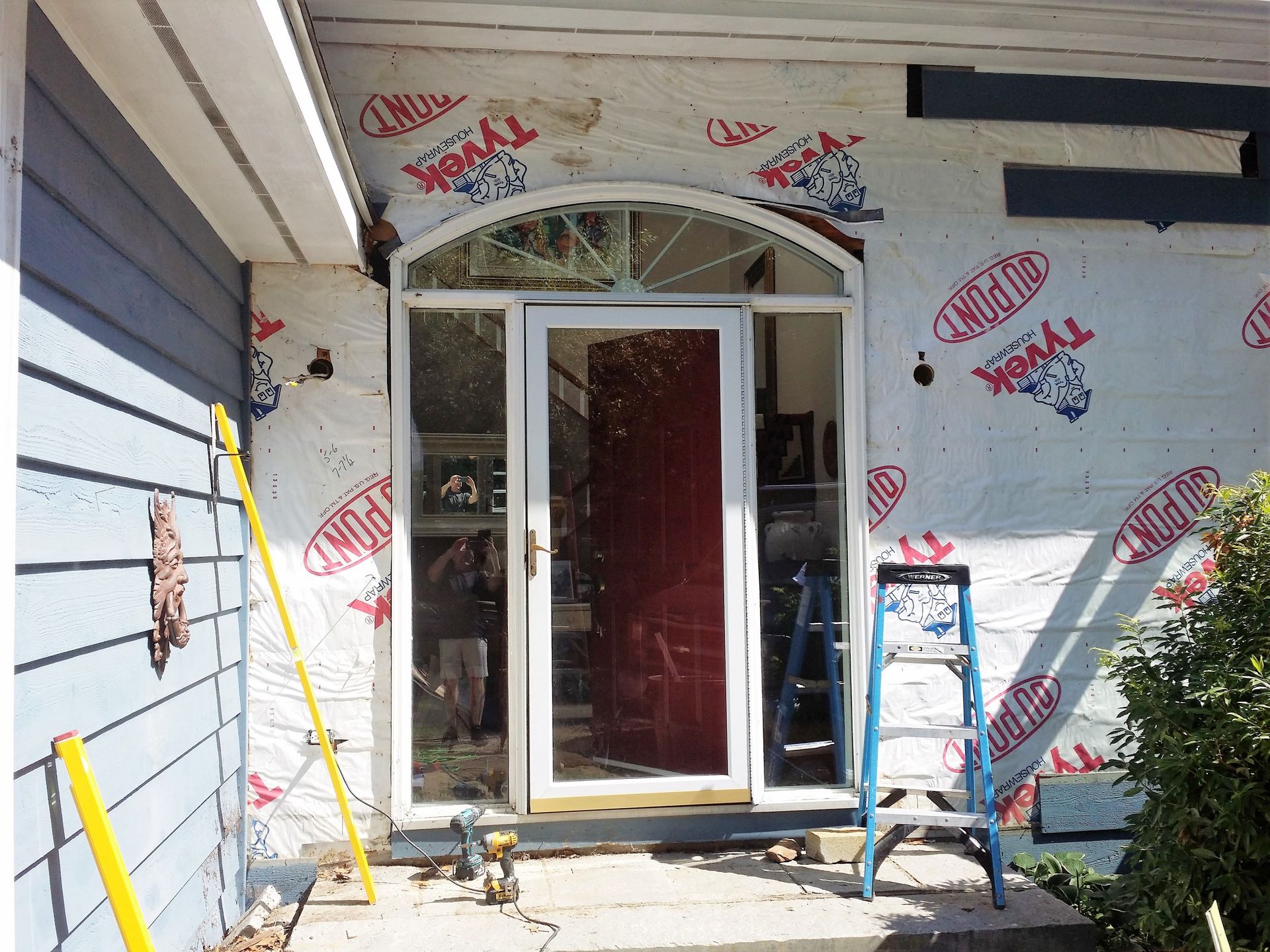 Front door remodel in progress: door frame exposed, covered in building wrap, tools nearby.