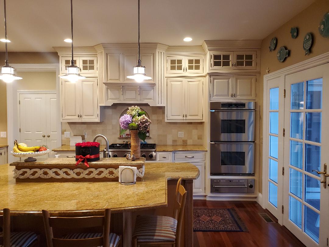 Kitchen with white cabinets, island with granite countertop, double oven, and french doors.