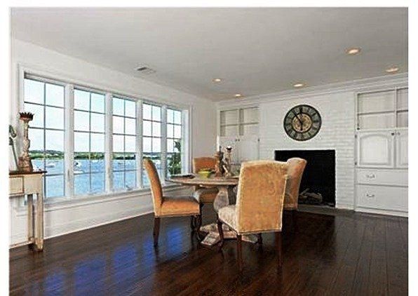 Dining room with a table and chairs, fireplace, large window overlooking water, dark wood floors.