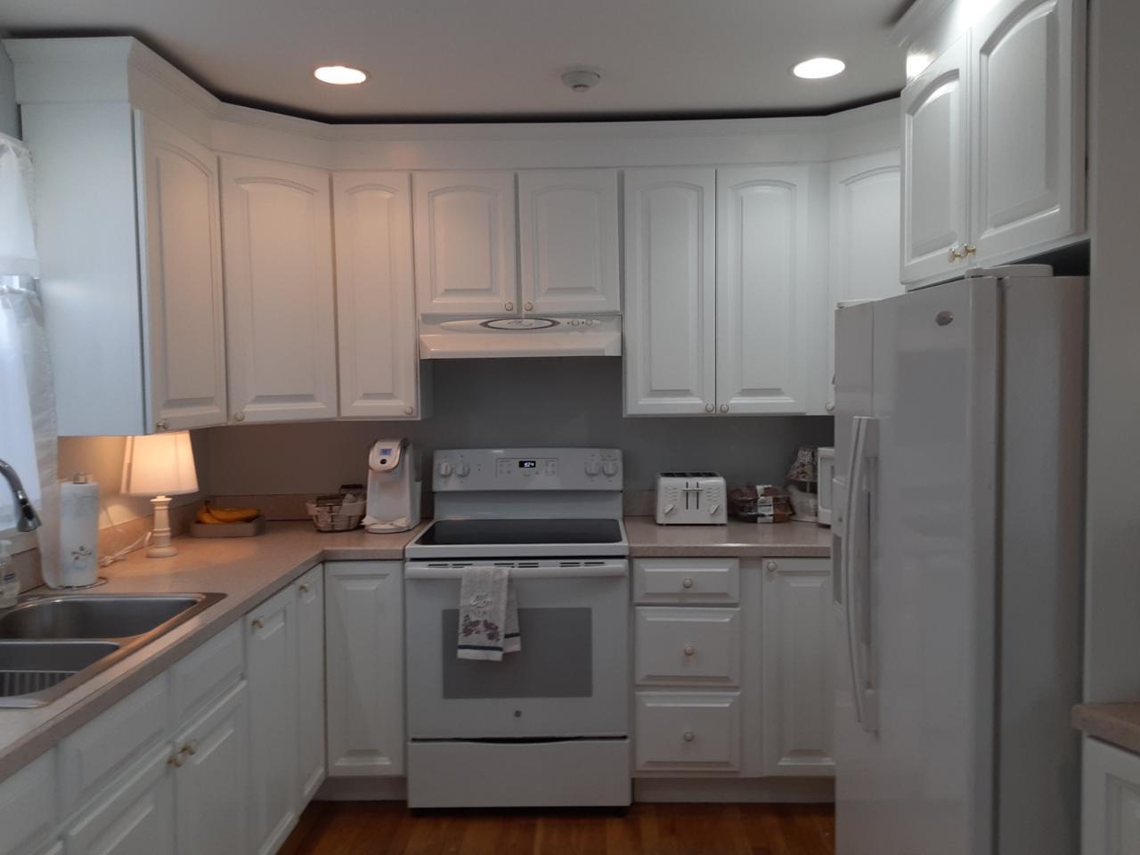 White kitchen with cabinets, appliances, and a sink, with light-colored countertops and wood flooring.