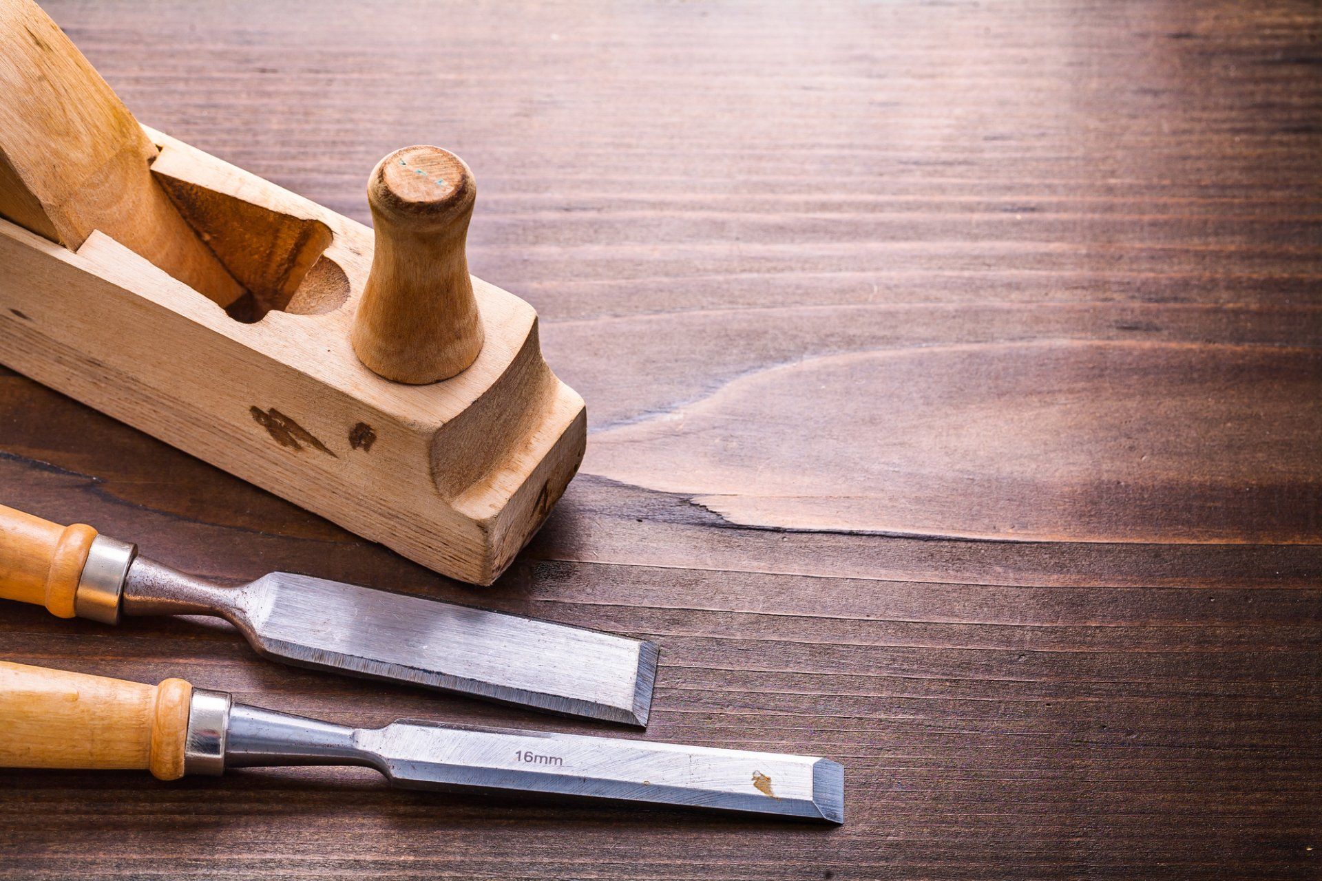 Woodworking tools: hand plane and two chisels on a wood surface.