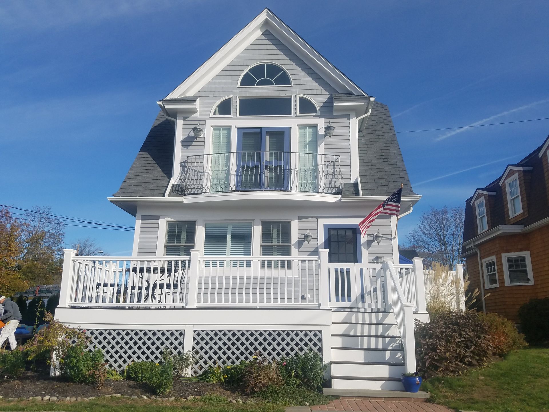Gray and white cottage with a balcony, American flag, and clear blue sky.