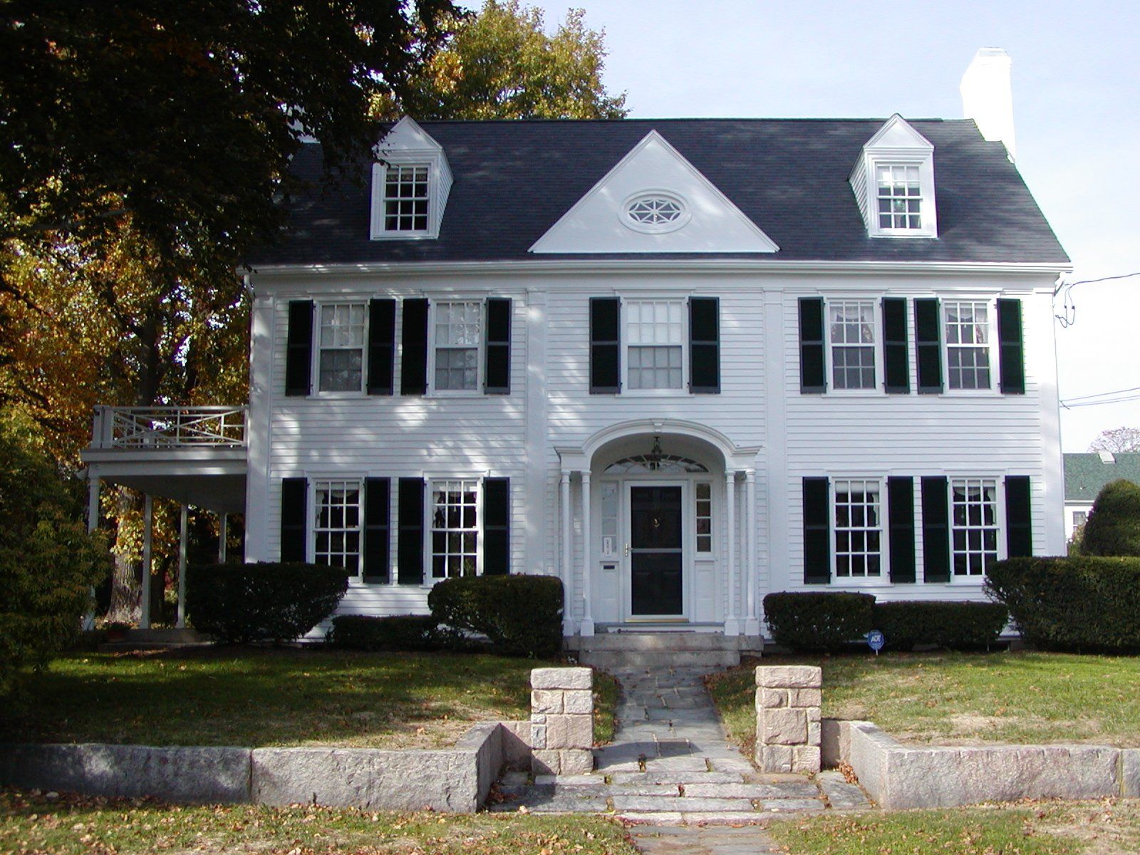 White colonial-style house with black shutters and a dark roof, a front porch, and manicured lawn.