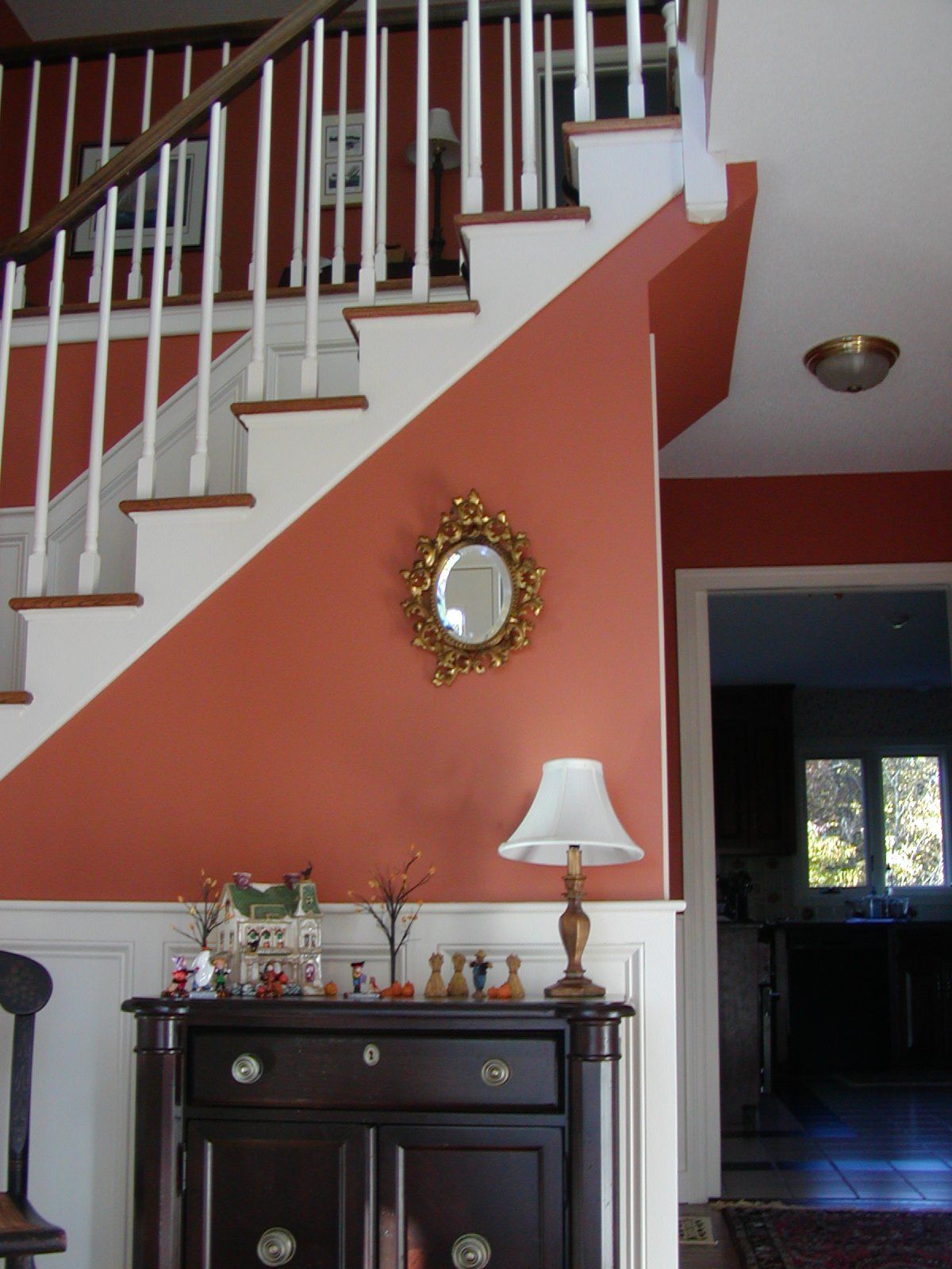 Entryway with staircase and terracotta-colored wall. A dark wood cabinet holds a lamp and decorative items.
