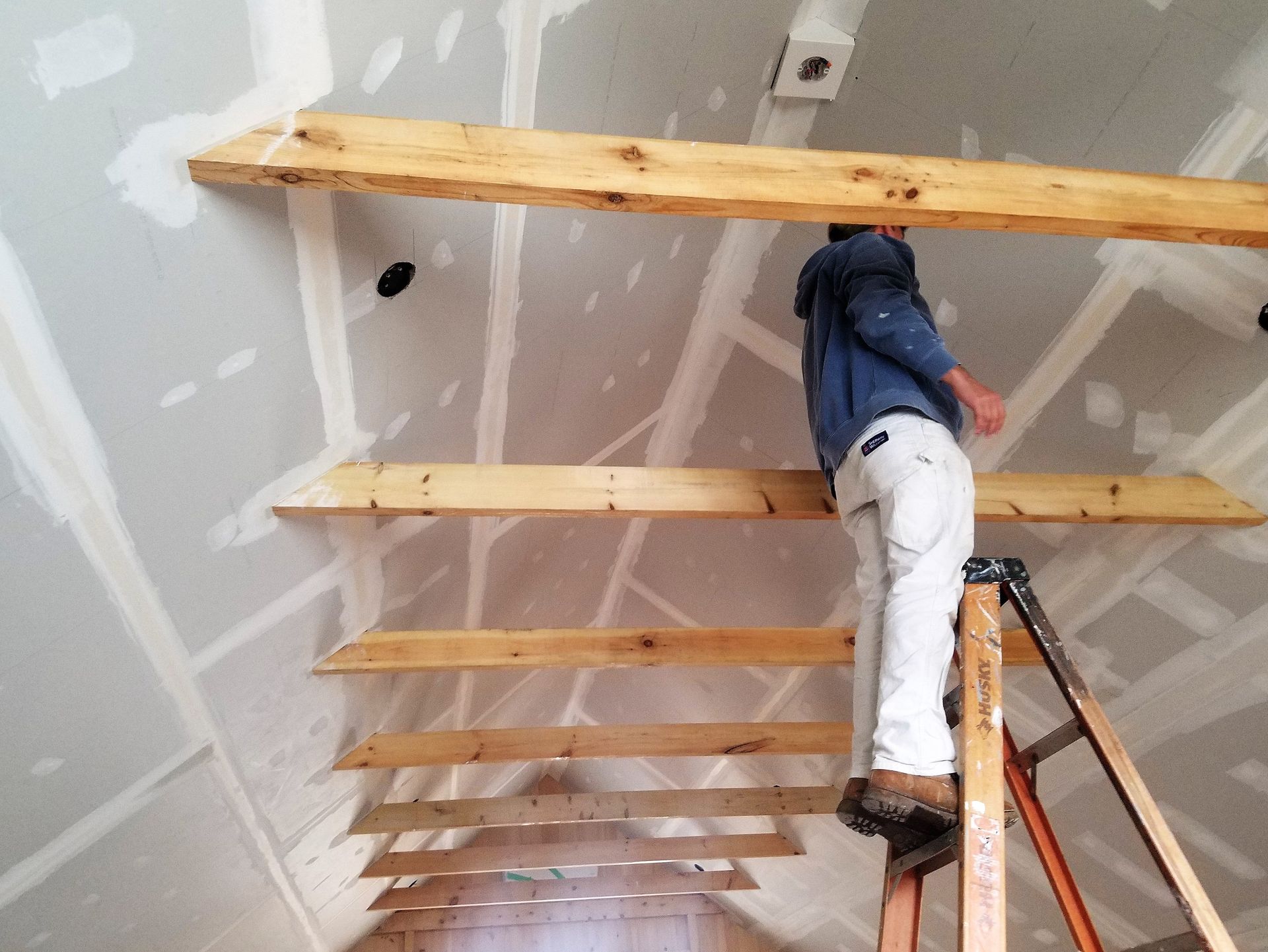 Person on ladder installing wooden beams on a drywall ceiling during construction.