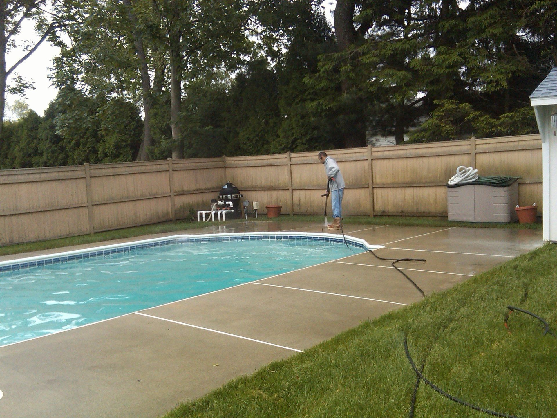 Person pressure washing the concrete pool deck in a backyard.