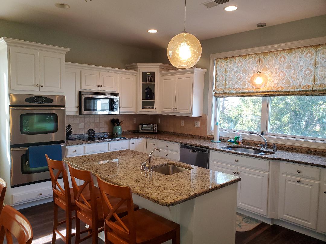 White kitchen with granite countertops and a center island, featuring stainless steel appliances.