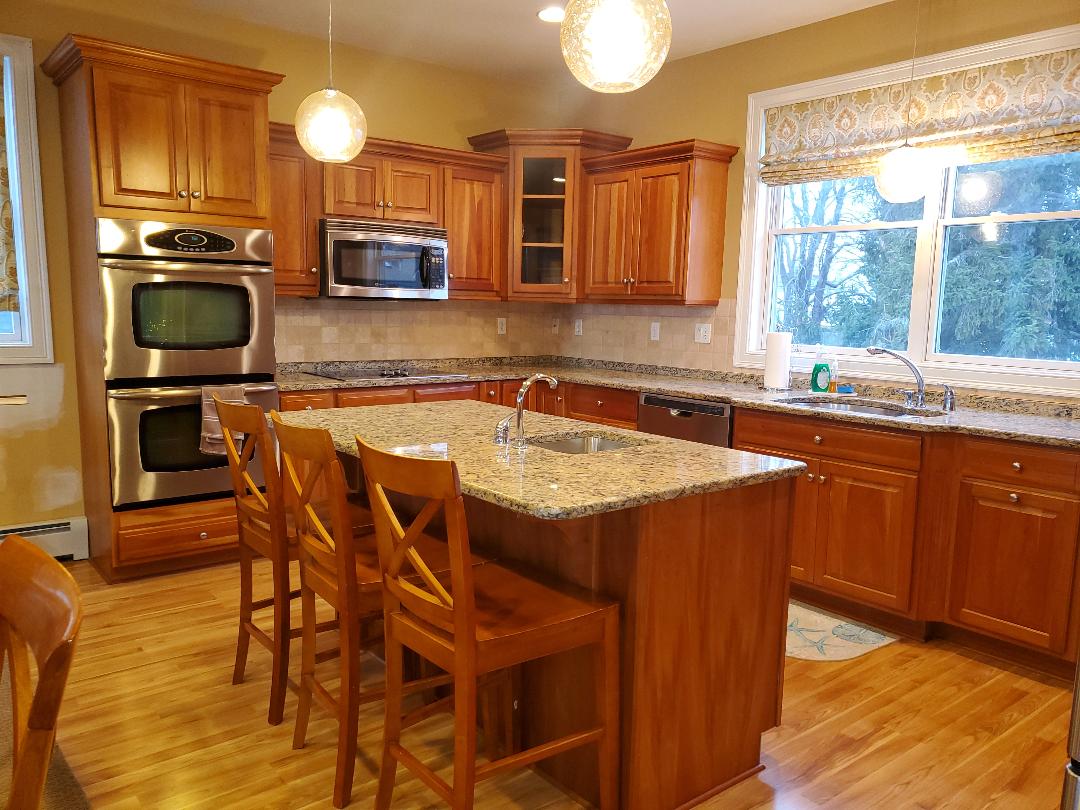 A kitchen with light brown cabinets, granite countertops, and a wooden island with seating.