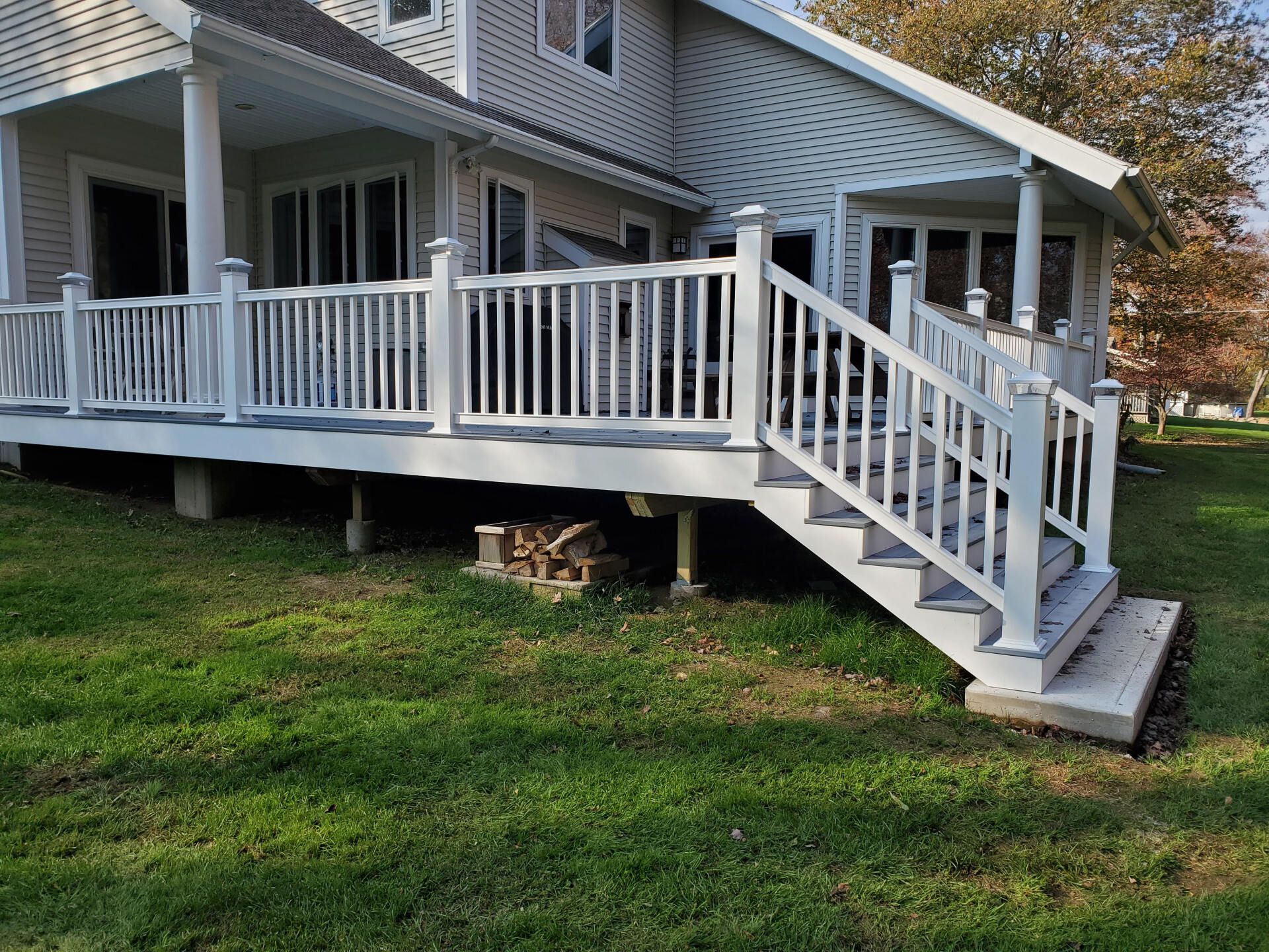 White deck with railing and steps in a grassy yard, attached to a two-story house.