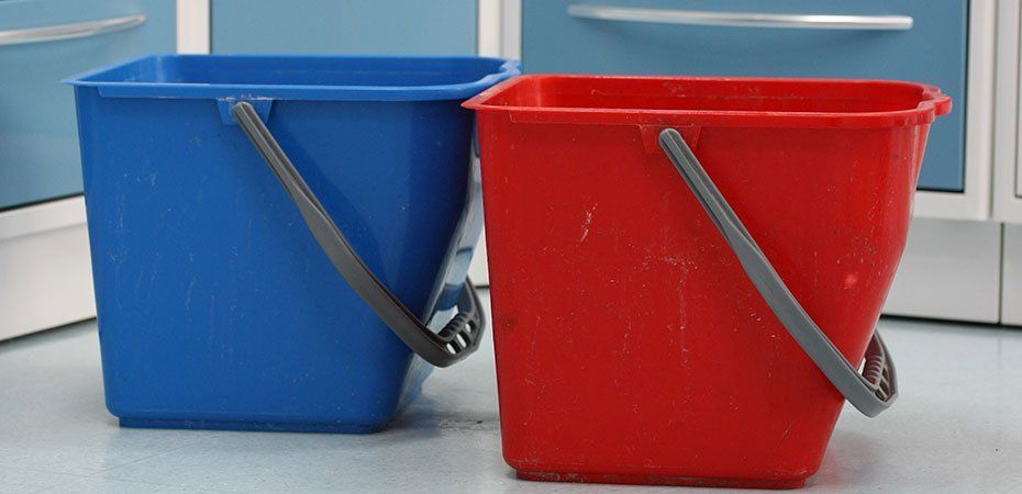 Zwei bunte quadratische Eimer, einer blau und einer rot, nebeneinander mit grauen Griffen.