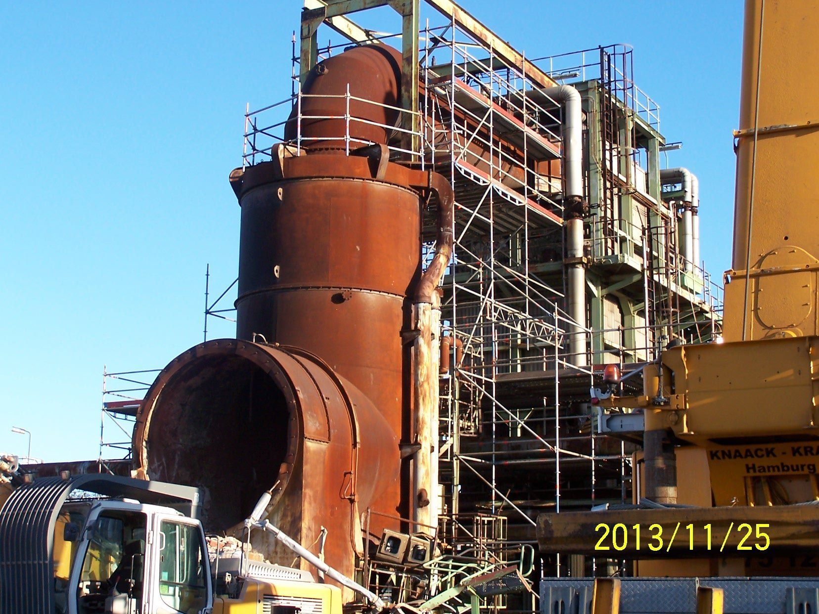 Rostige Industriemaschinen mit Gerüsten, blauer Himmel im Hintergrund.