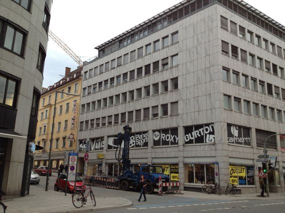 Gebäude mit mehreren Stockwerken und Ladenfronten; Straße mit Baustellen, Fahrrädern und Fußgängern.