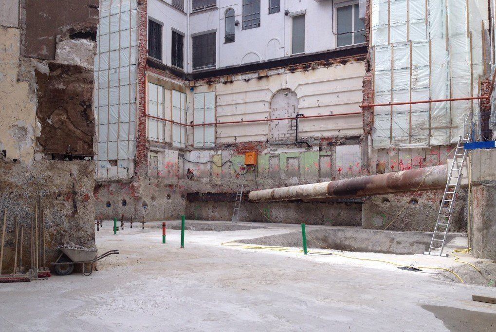 Baustelle mit freiliegenden Ziegelwänden, Dämmung und Rohrleitungen; unbefestigter Boden.