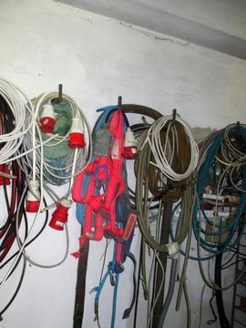 Aufgerollte elektrische Kabel und Leitungen hängen an Haken an einer weißen Wand; rote und weiße Stecker sind zu sehen.