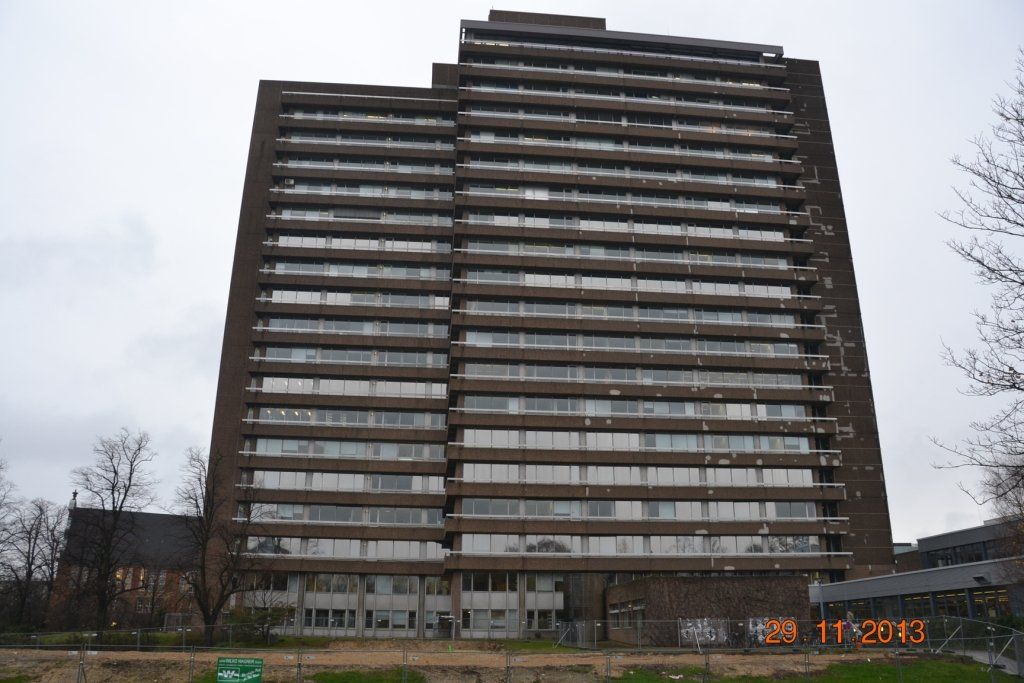 Hohes, braunes Wohnhaus aus Beton mit vielen Fenstern unter einem bewölkten Himmel.
