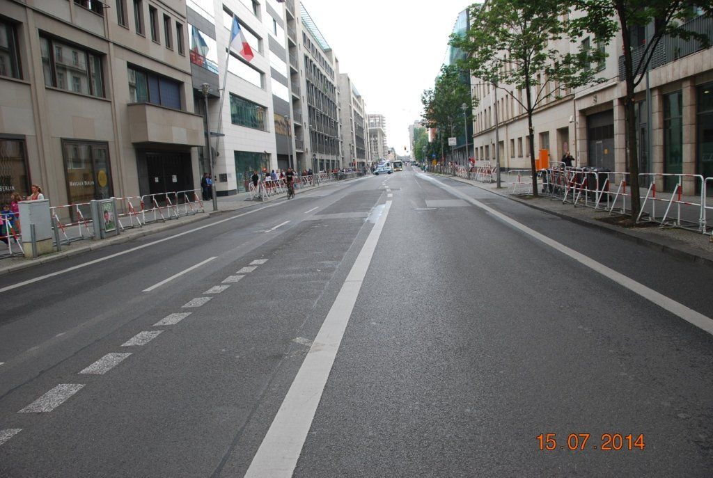 Straßenansicht mit Gebäuden, Mittellinie und Fußgängerbarrieren auf beiden Seiten.