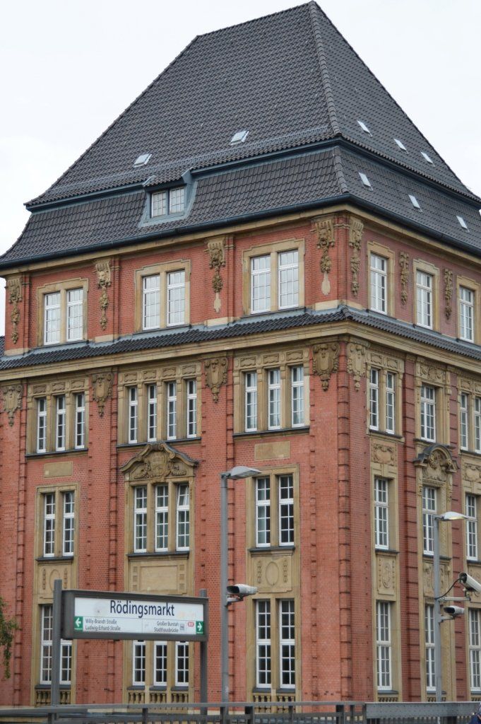 Rotes Backsteingebäude mit dunklem Ziegeldach, mehreren Fenstern und dekorativen Steinelementen. 