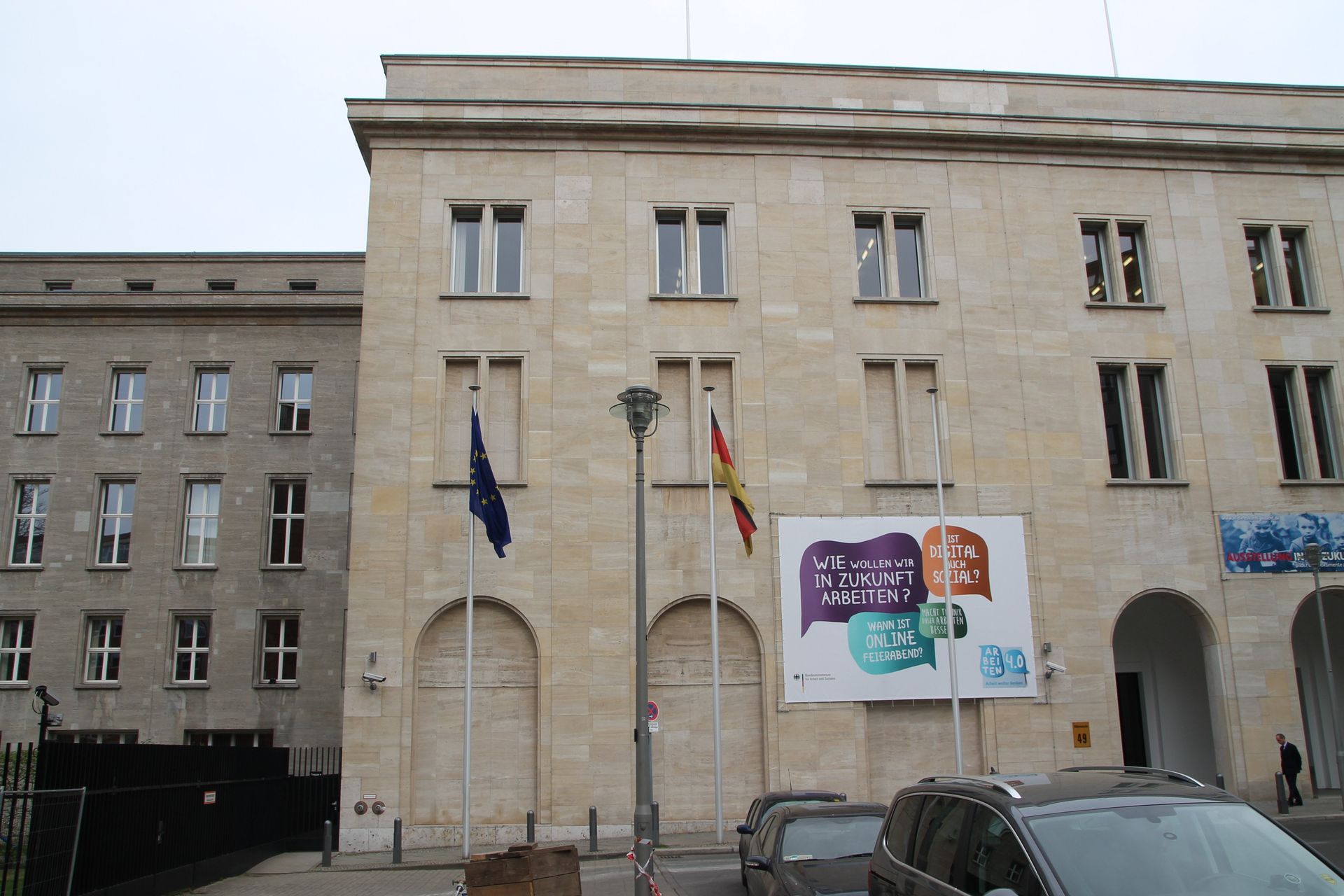 Gebäude mit Flaggen: EU, Spanien; ein Plakat, Autos und Menschen auf der Straße.
