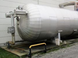 Großer, silberner, zylindrischer Speichertank mit angeschlossenen Rohren und Ventilen, im Freien.