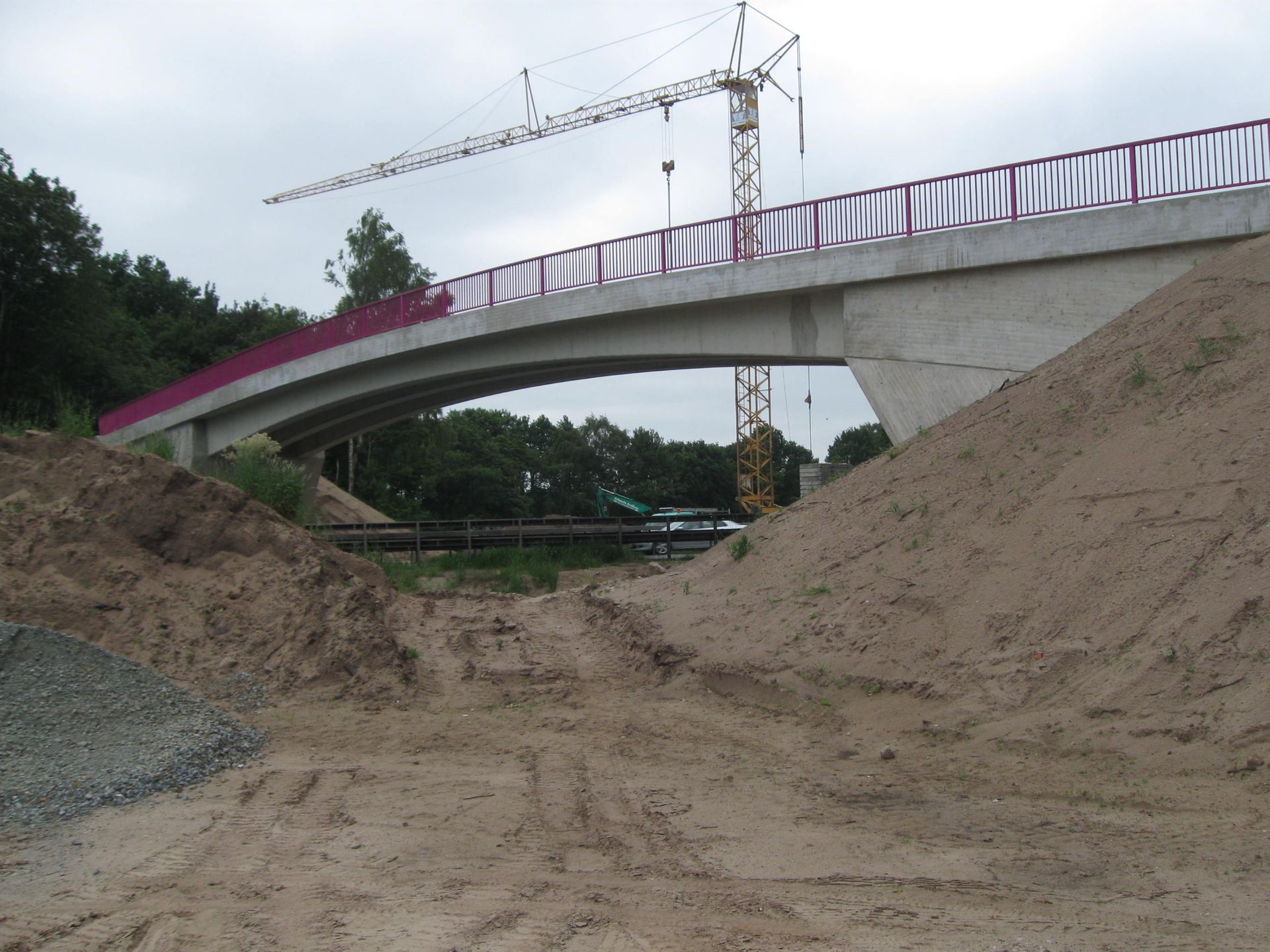 Brücke im Bau, darüber ein Kran, im Vordergrund Sandhaufen.